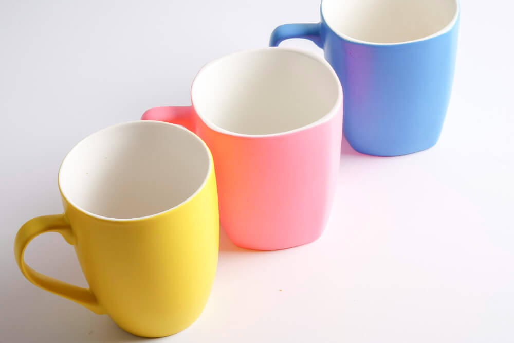 A cup with three color variations: yellow, pink, and blue